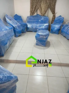 "مجموعة من الأثاث المغلف بالكامل بالبلاستيك الأزرق في غرفة ذات أرضية سيراميك وستائر بنية."