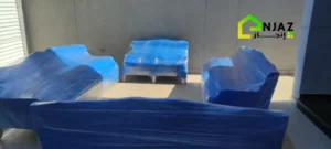 مجموعة من الأرائك المغلفة بالبلاستيك الأزرق لحمايتها أثناء النقل، معروضة في منطقة خارجية مضيئة