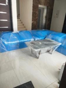 مجموعة من الأرائك والطاولة مغلفة بالبلاستيك موضوعة في مدخل منزل.